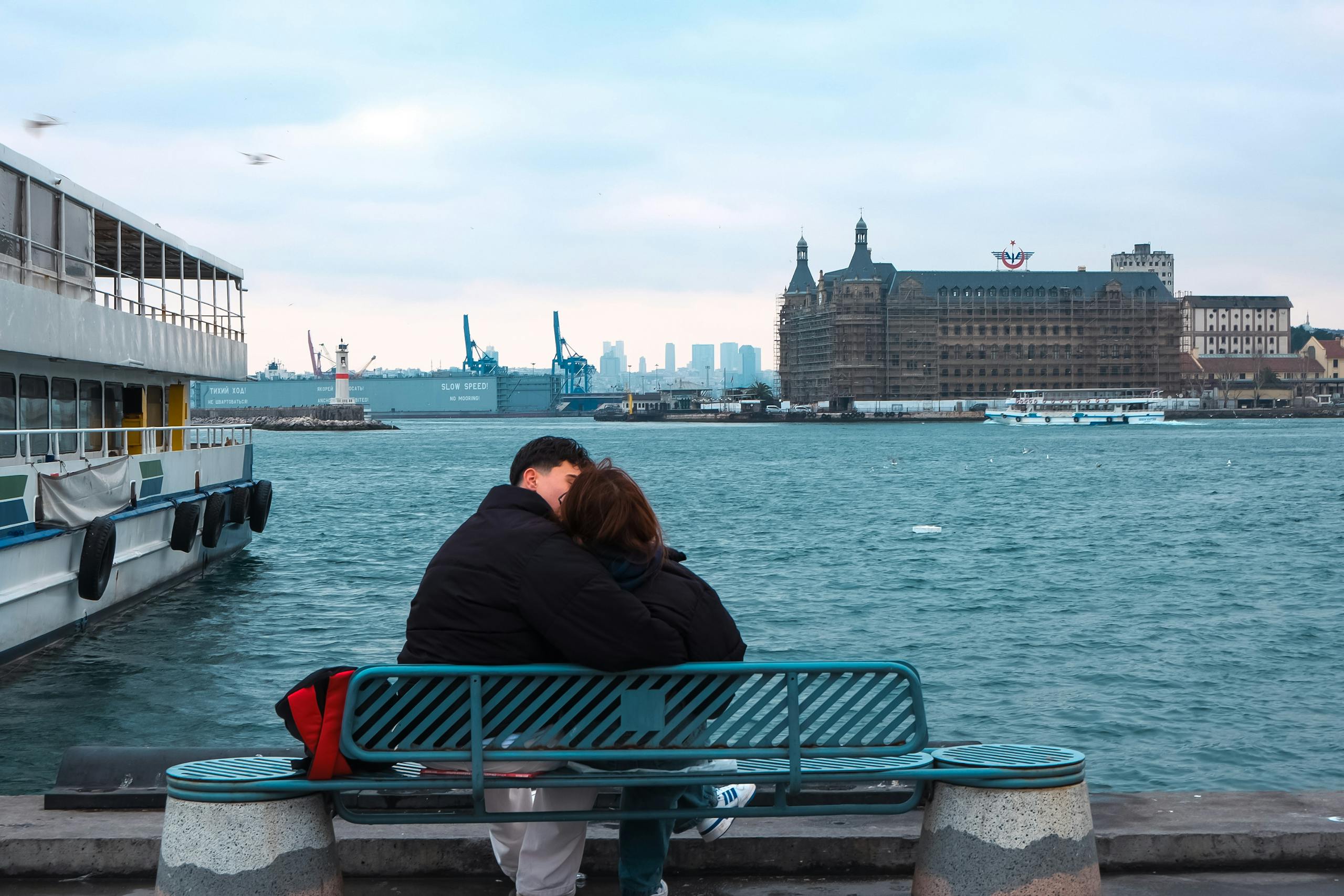 A couple embraces on a bench overlooking the Bosphorus with a historic Istanbul landmark.